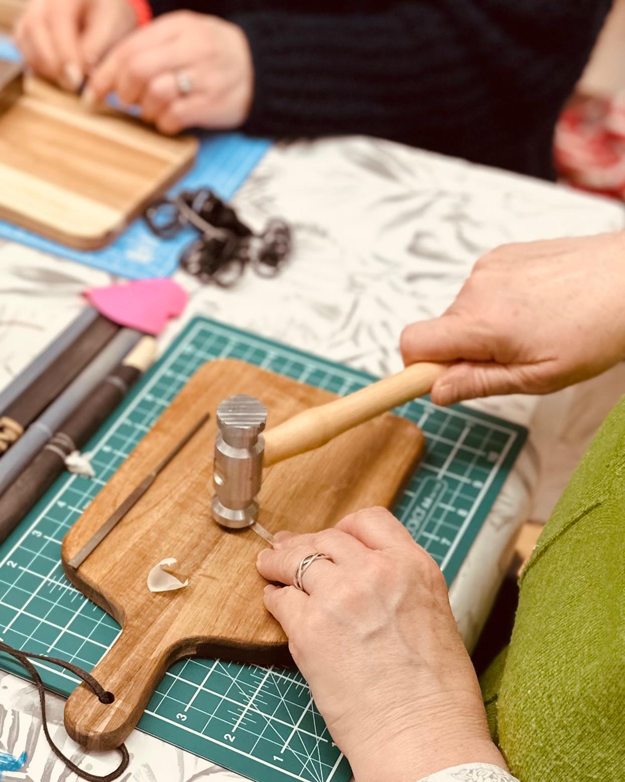 A person is crafting an adjustable silver ring on a workshop table, using tools to shape and texture the metal.