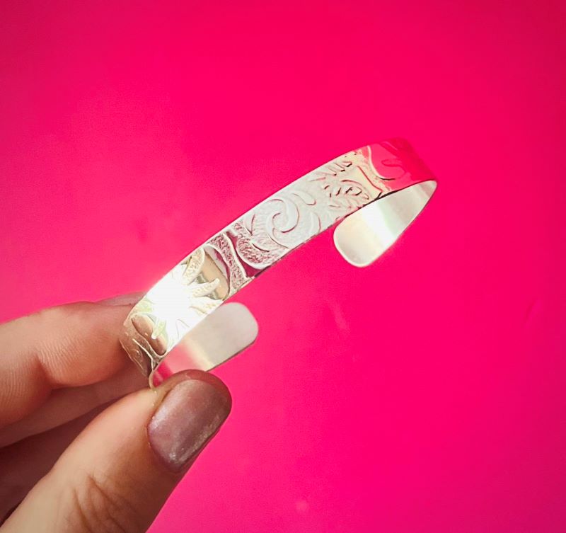 Hand holding a wide silver cuff with floral pattern texture against a pink background | Silverlicious Artisan Jewellery