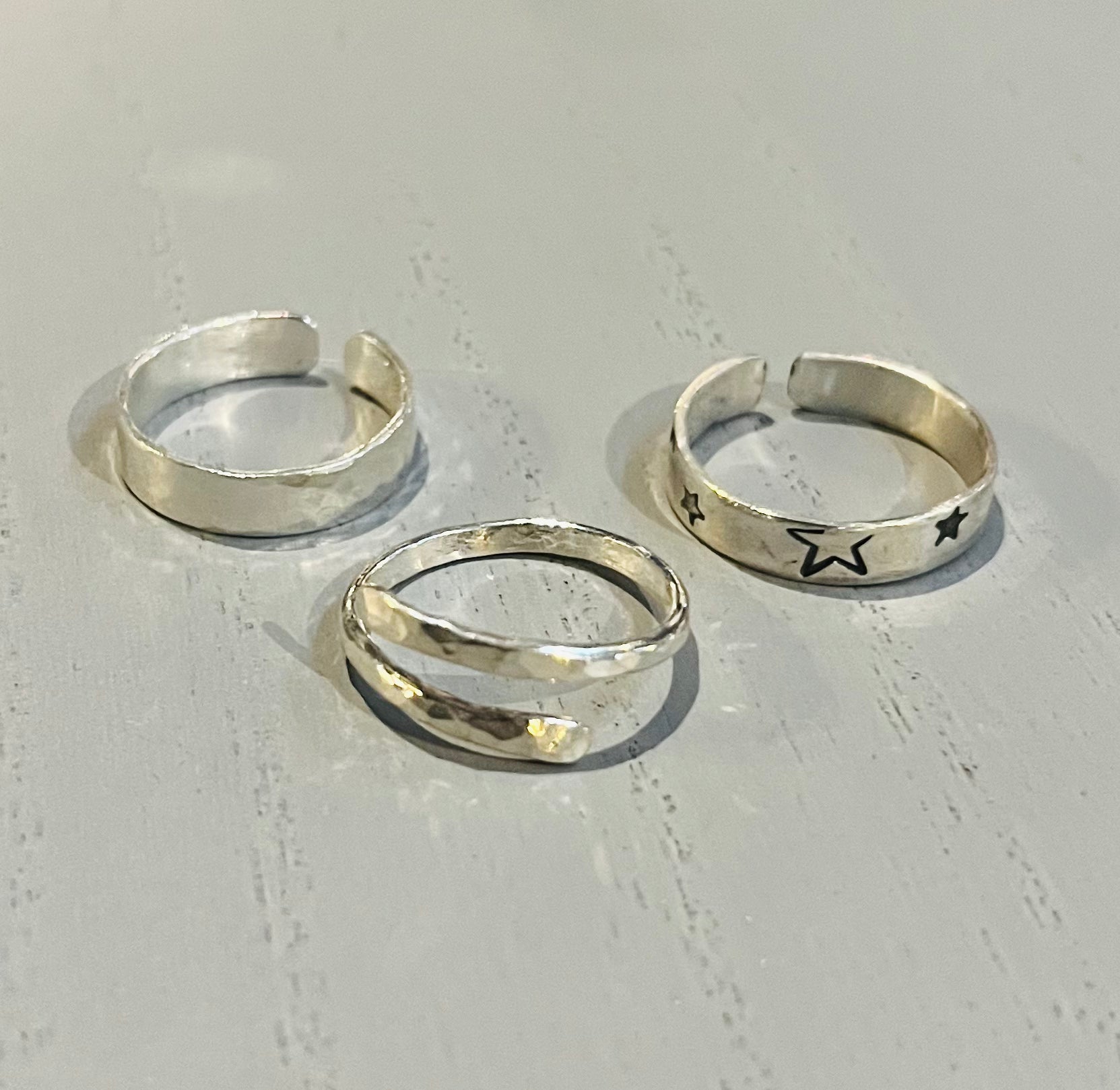 Three adjustable silver rings with different textures and one with a star design, displayed on a light background.