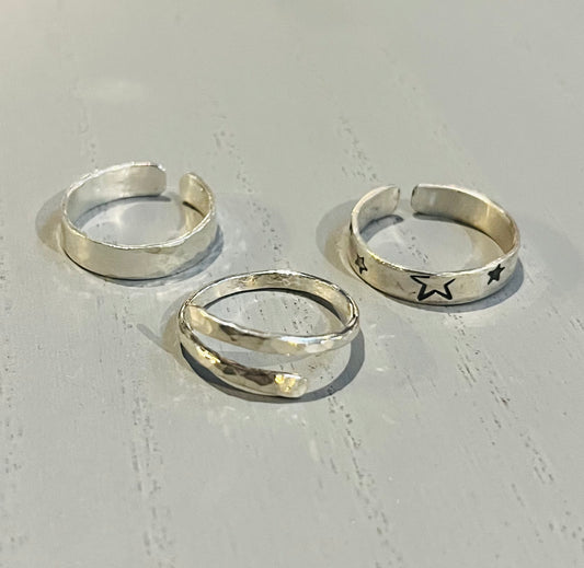 Three adjustable silver rings with different textures and one with a star design, displayed on a light background.
